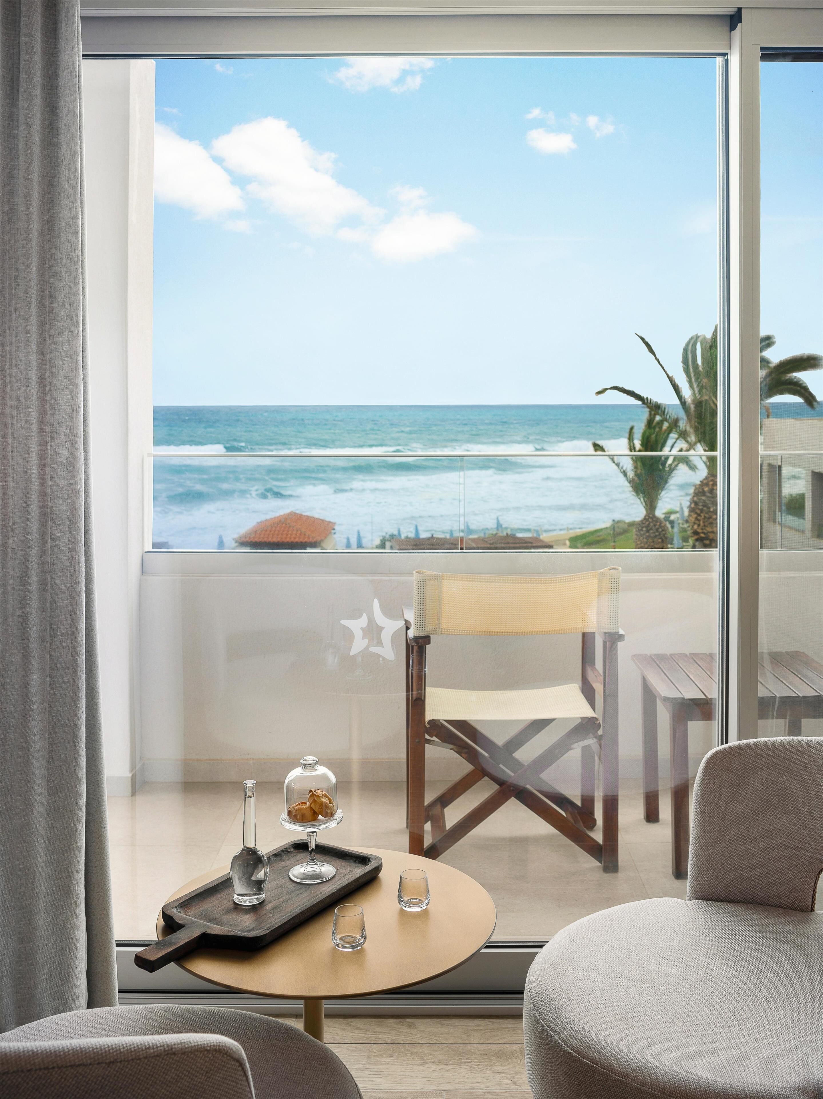 Un balcón con vista al océano, una silla, una pequeña mesa con vasos y un objeto decorativo sobre la mesa.