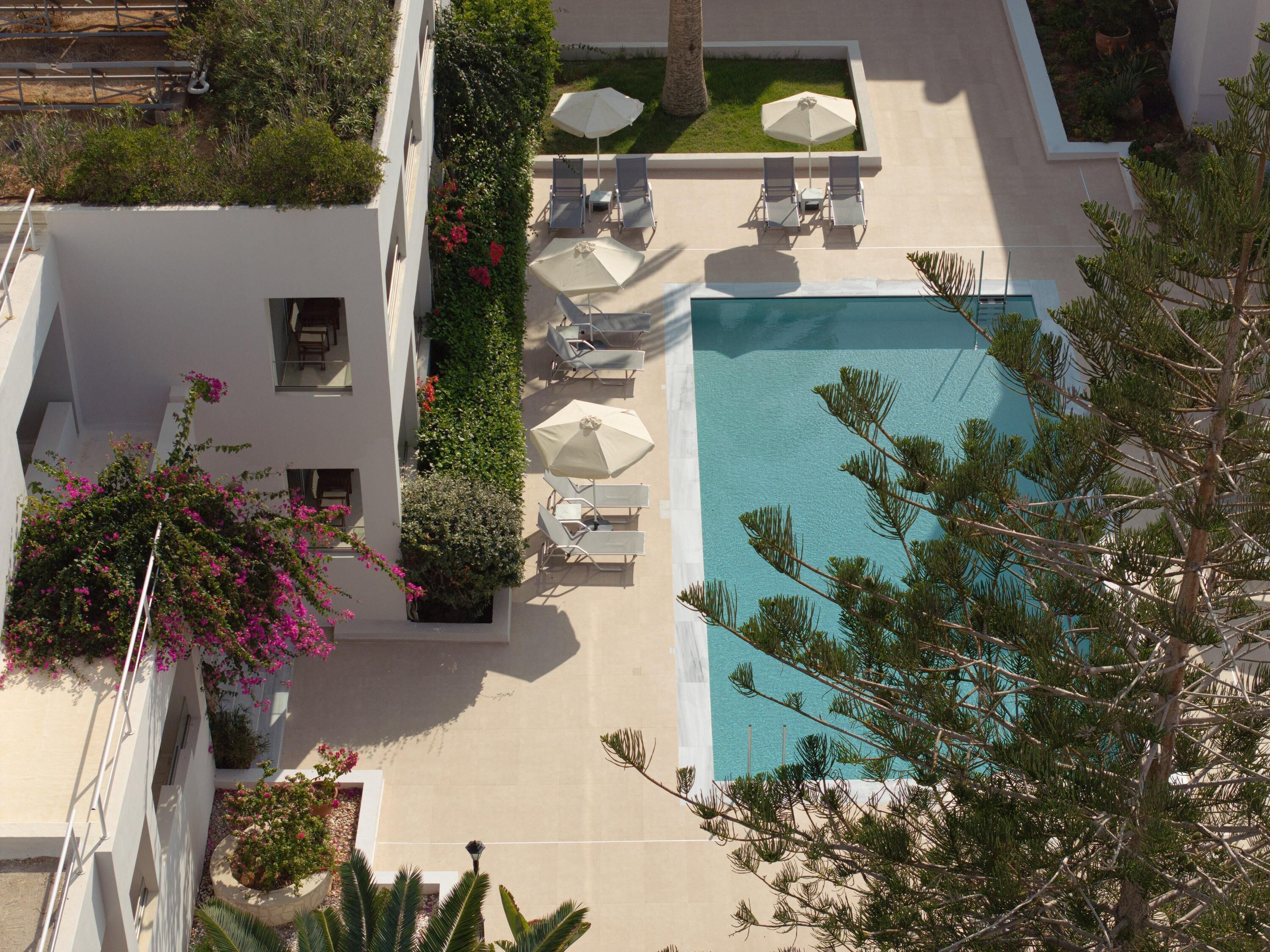 An aerial view of a hotel with a swimming pool, lounge chairs, and a garden area.