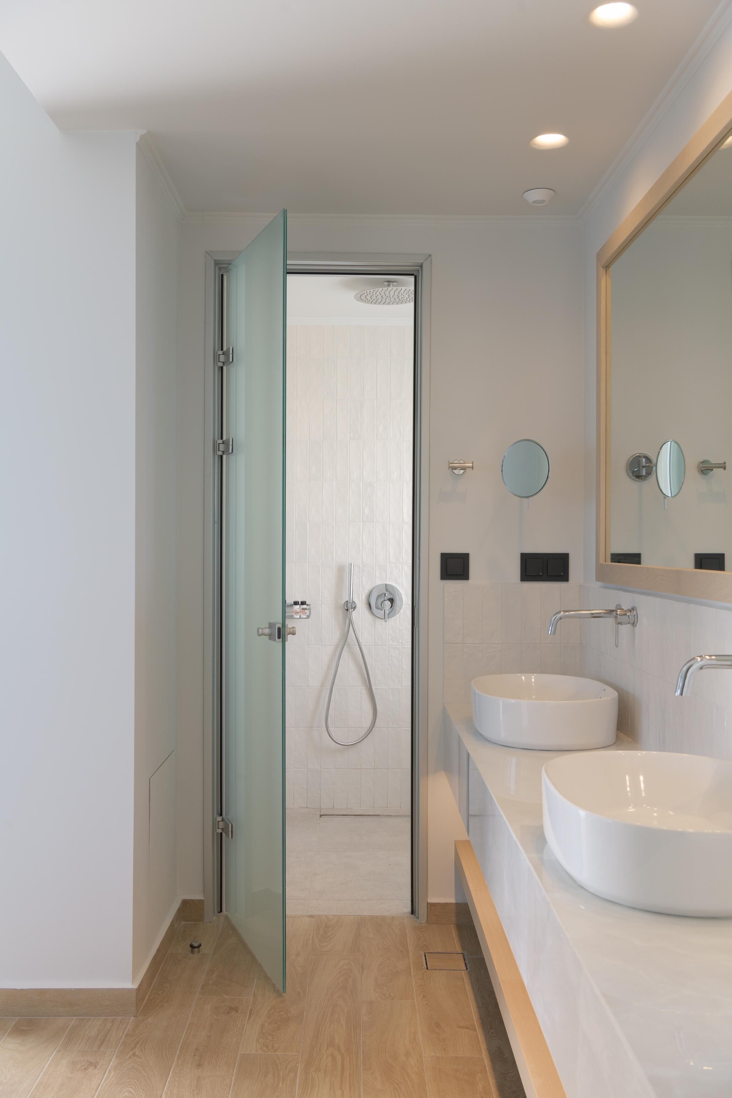 A modern bathroom with a glass shower door, two sinks, and a large mirror.