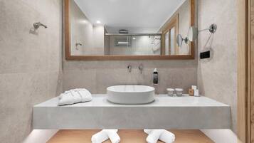 Un baño moderno con un espejo grande, un lavamanos redondo y dos toalleros.