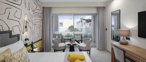 A hotel room with a bed, a desk, a chair, a table with a bottle and glasses, and a view of the outside.