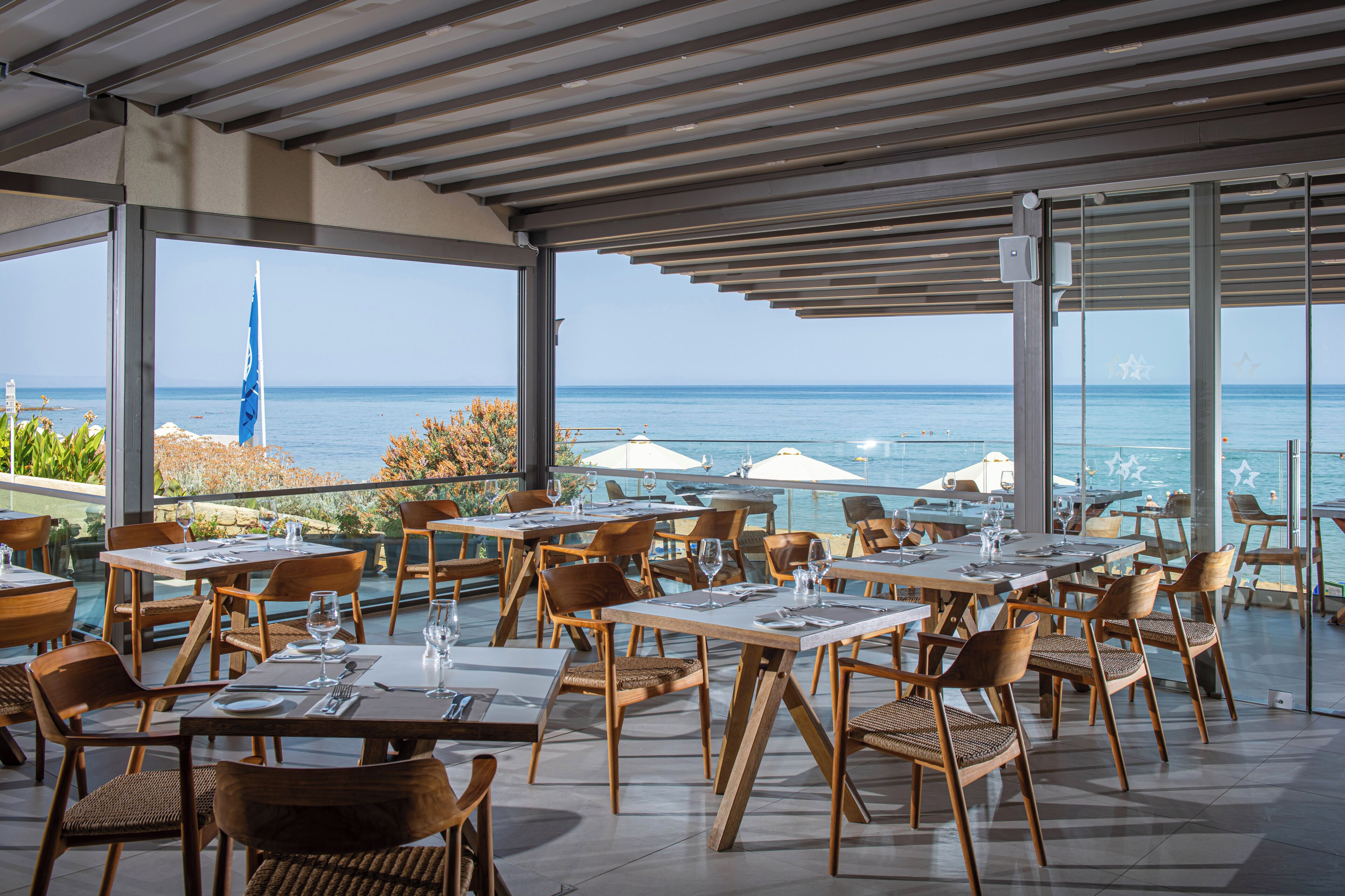 An outdoor dining area with tables and chairs, overlooking a body of water and a distant tower.