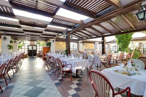 A spacious outdoor dining area with multiple tables set for dining, surrounded by red chairs, under a wooden pergola with natural light. - Creta Royal - Adults only (Rethymno)