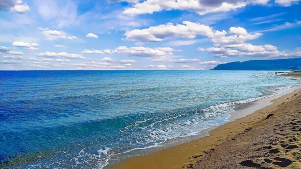 A beach with clear blue water and a sandy shore.