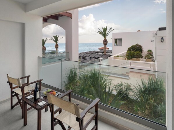 A balcony with a table and chairs, overlooking a coastal area with palm trees and a view of the sea. - Creta Royal - Adults only (Rethymno)