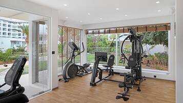 A modern gym with cardio machines and free weights, large windows with a view of greenery and buildings.