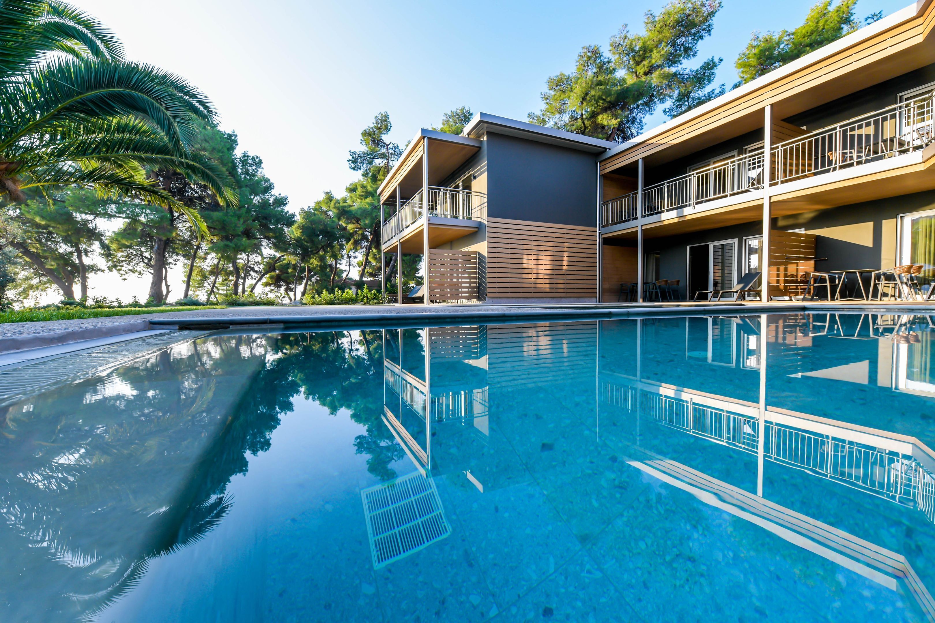 A modern hotel with a pool, balconies, and a lush green environment.