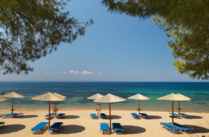 A beach with blue lounge chairs and straw umbrellas, a clear sky, and the ocean in the background. - Blue Dolphin Hotel (Polygyros)