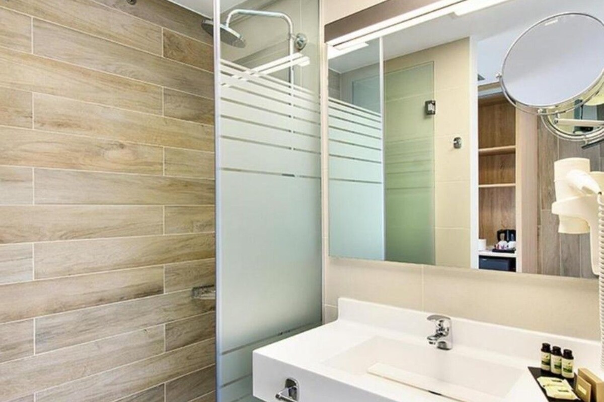 A modern bathroom with a wooden floor, a white sink, a large mirror, and a shower area.