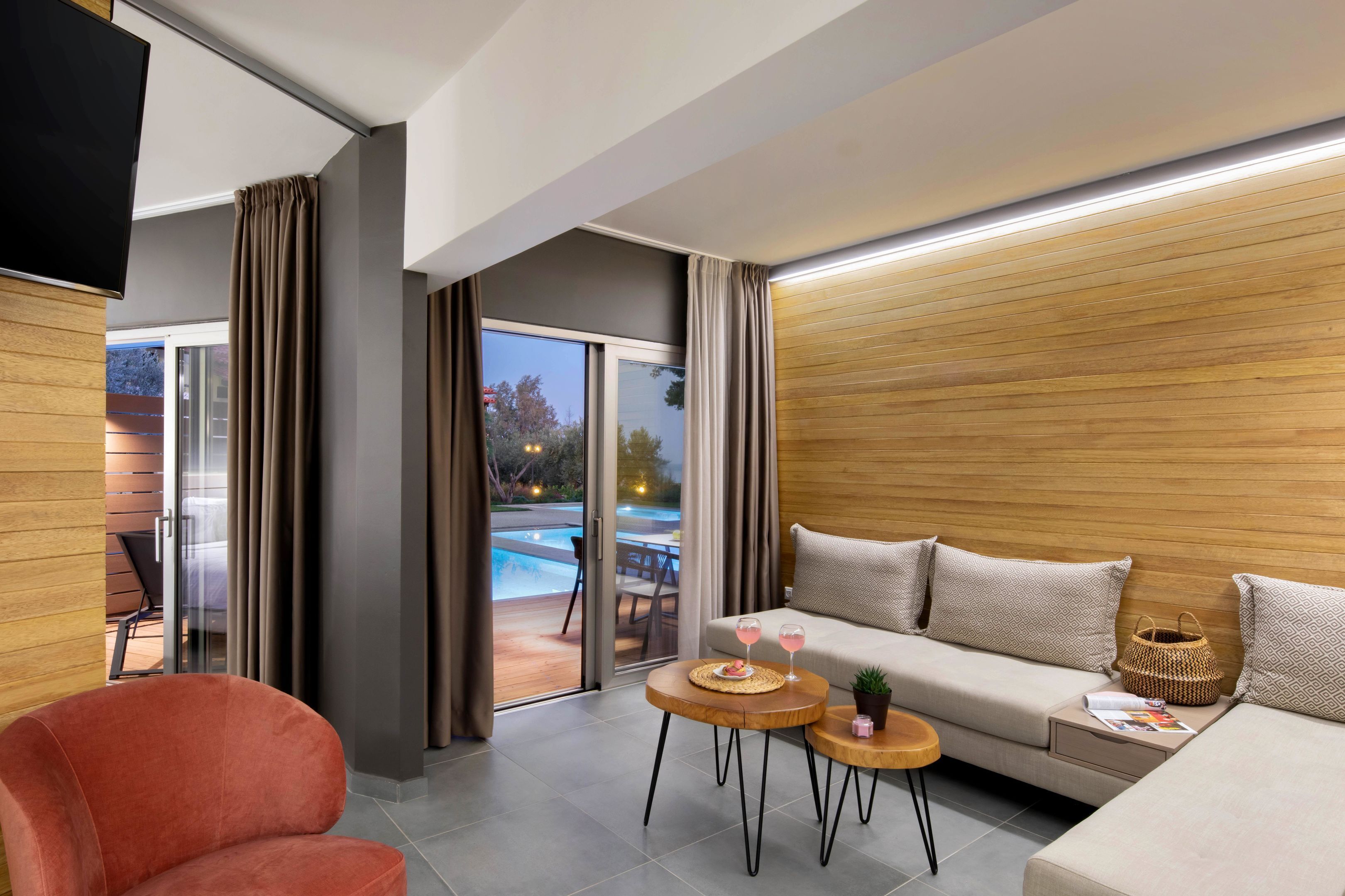 Una sala de estar moderna con un sofá, un sillón rojo y una mesita con bebidas.