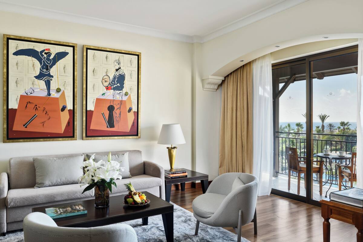 A hotel room with a balcony, a sofa, a coffee table, and a dining area.