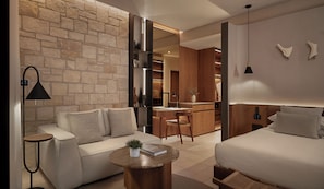 A modern hotel room with a stone wall, a sofa, a desk, a bed, and a small coffee table with a plant.
