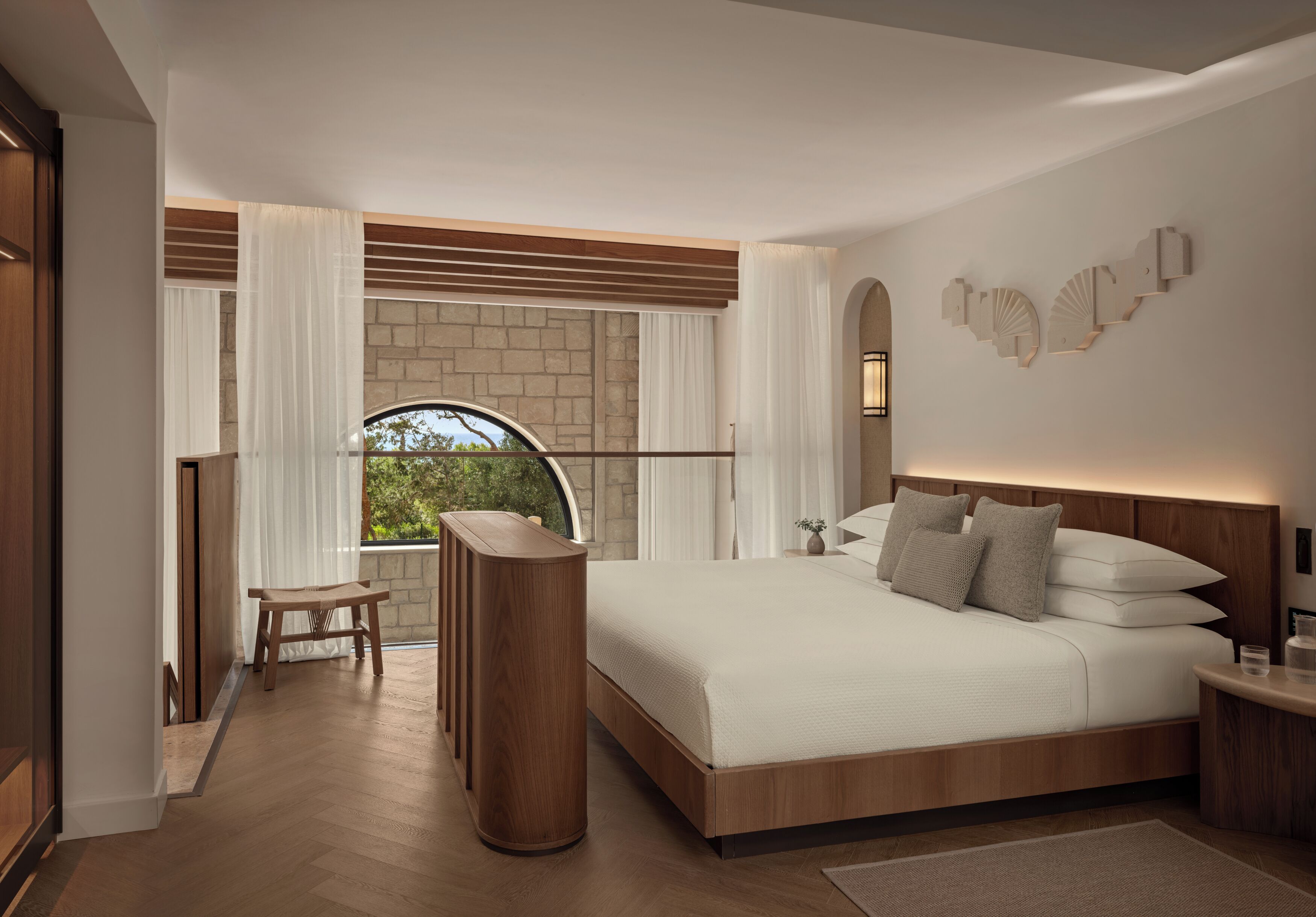 Ein modernes Schlafzimmer mit einem großen Bett, einem kleinen Tisch, einer Holzbank, einer Steinwand und einem Fenster mit Vorhängen.