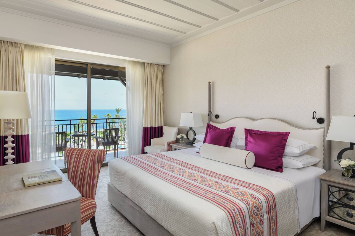 A hotel room with a bed, a desk, a chair, a nightstand, and a view of the ocean.