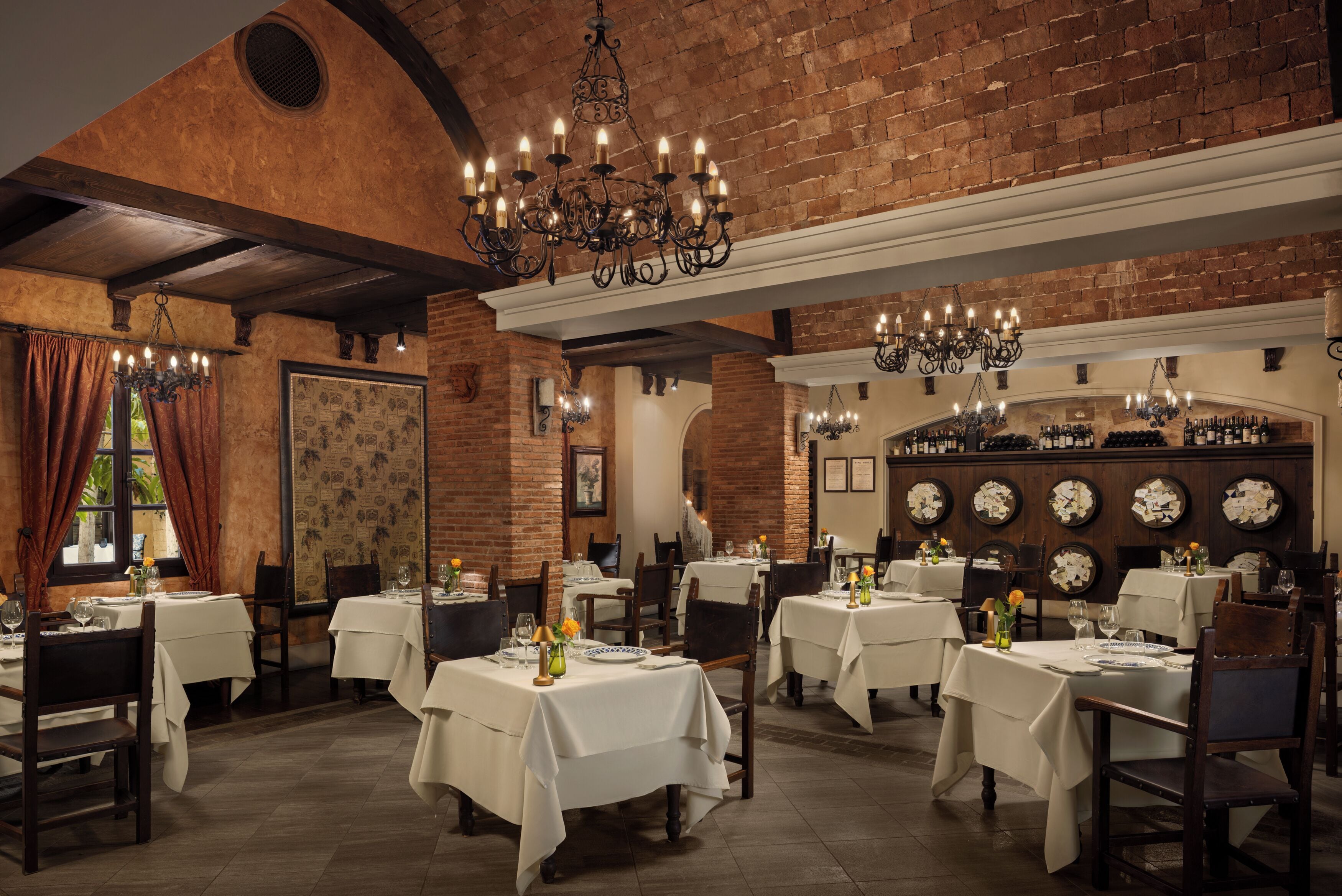 A restaurant with brick walls, chandeliers, and white tablecloths.