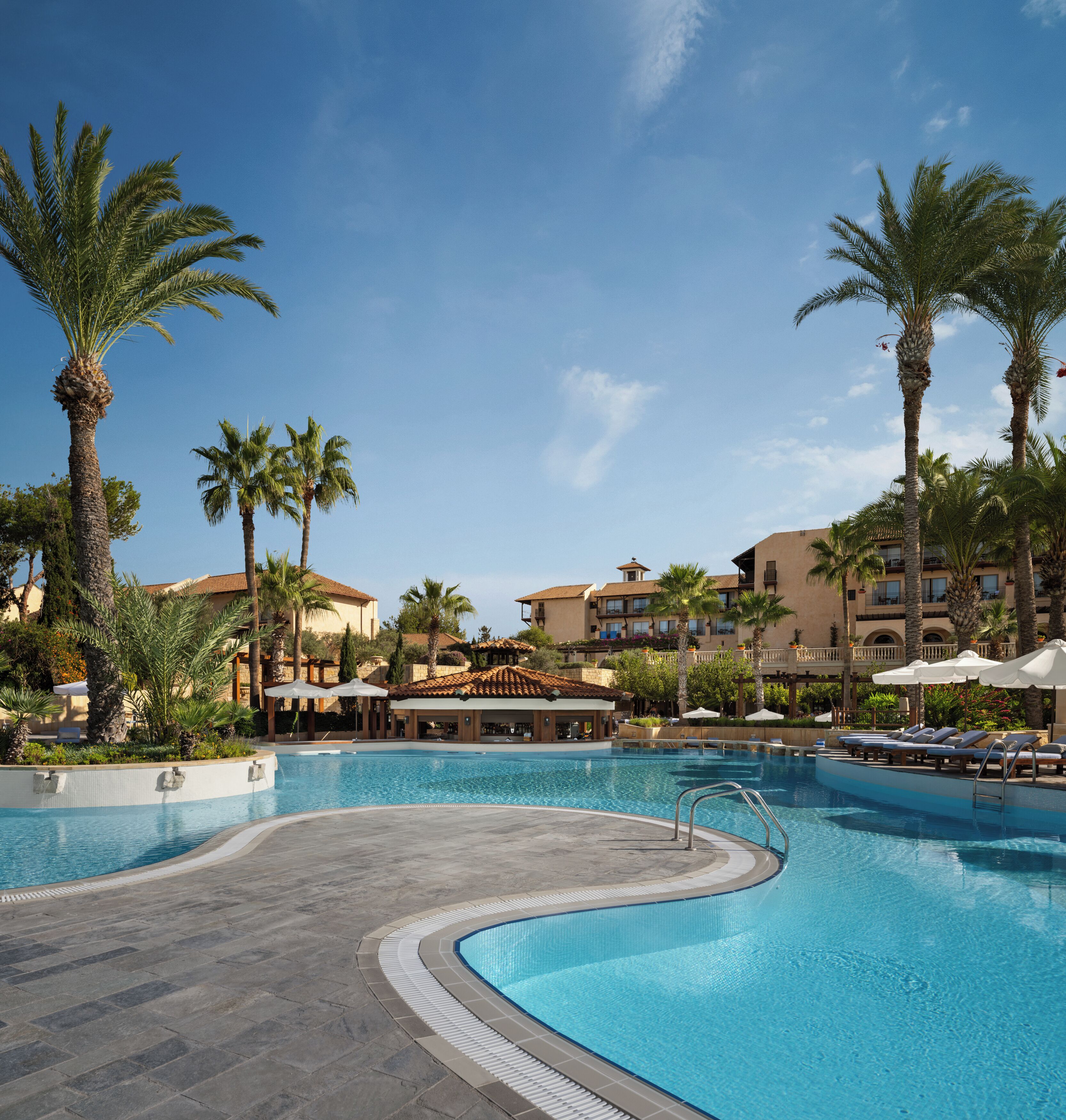 A resort pool with palm trees, lounge chairs, and a building with balconies.
