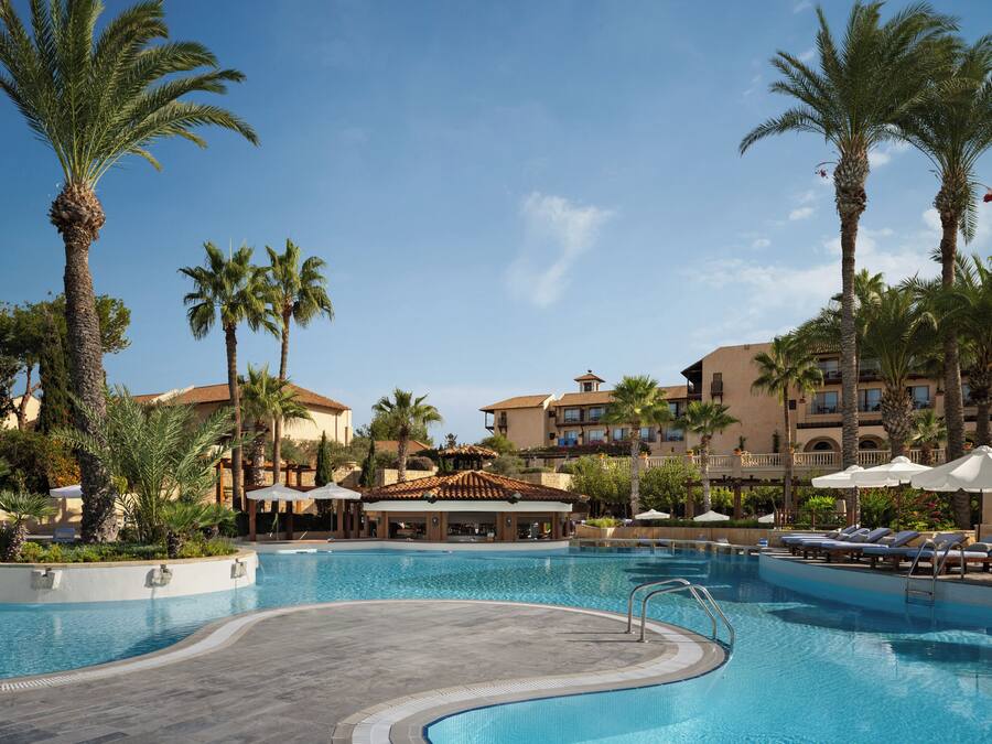 Una piscina de resort con palmeras, sillas de descanso y un edificio con balcones.