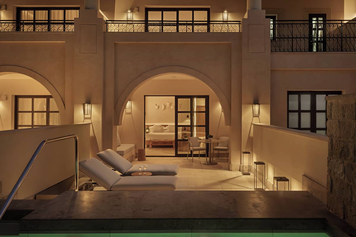 A pool area with lounge chairs and a bedroom visible through an arched doorway.