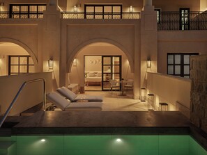 A pool area with lounge chairs and a bedroom visible through an arched doorway.