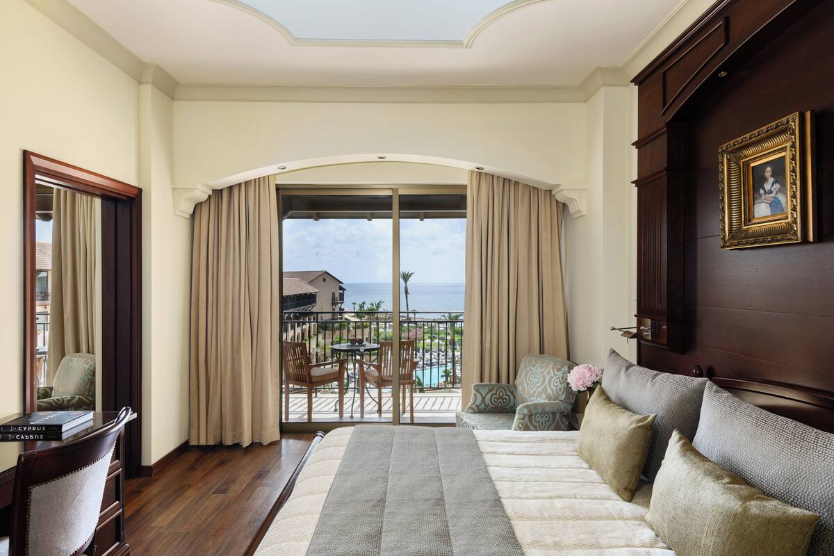 A hotel room with a balcony, a bed, a desk, and a view of the ocean.