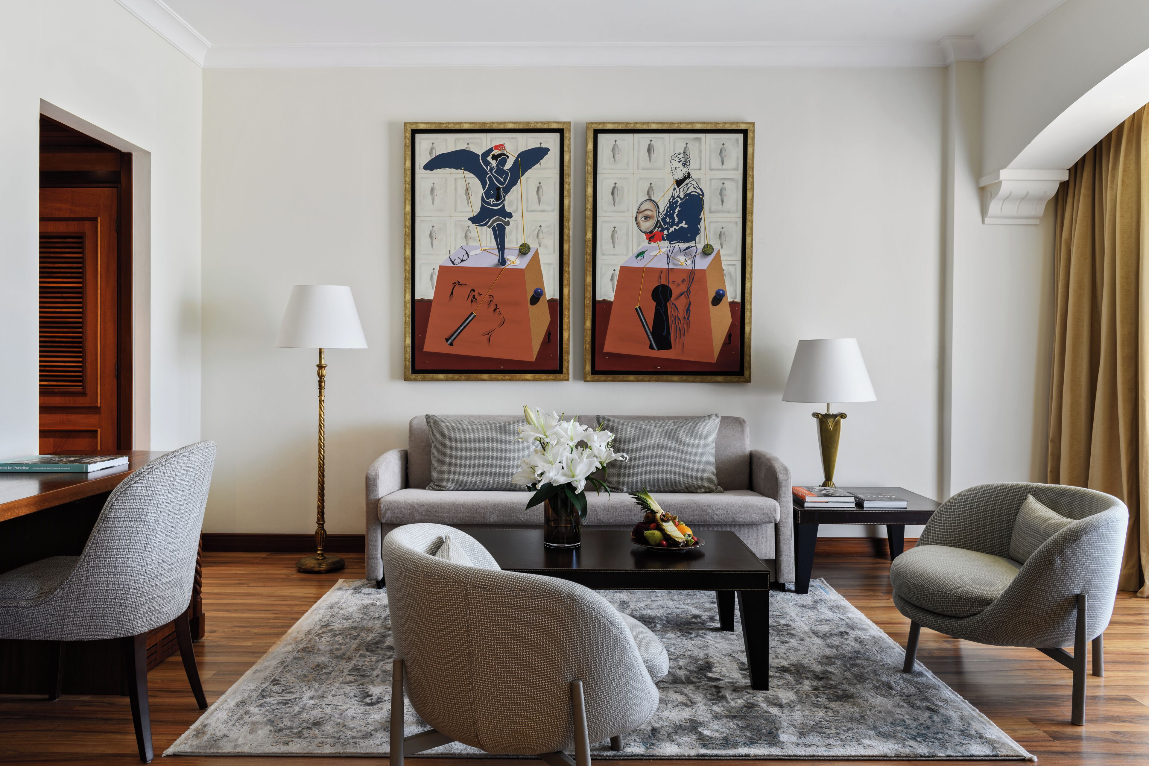 Una sala de estar moderna con un sofá, dos sillones, una mesa de centro y dos obras de arte enmarcadas en la pared.