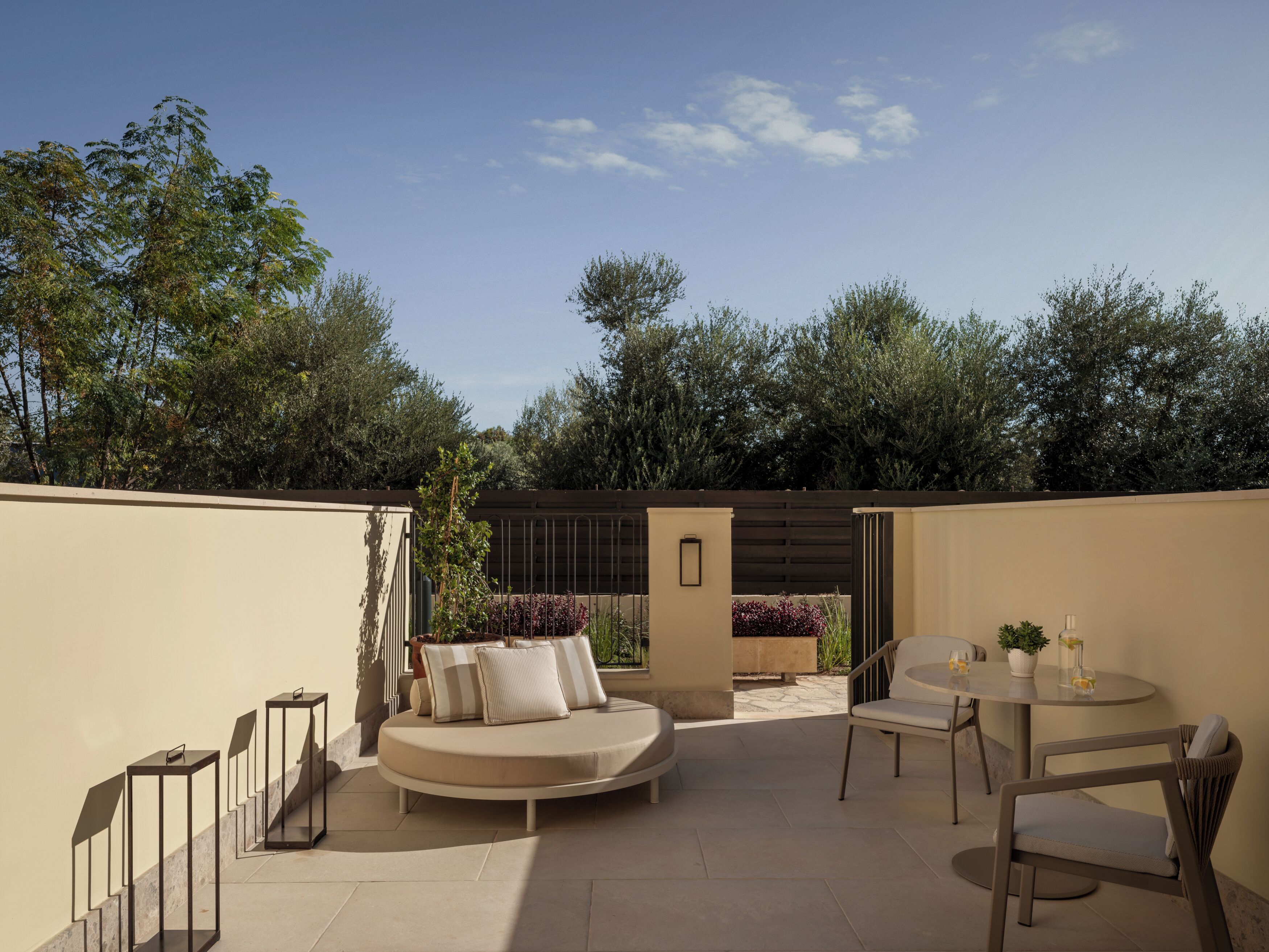 A patio with a sofa, chairs, and a table, surrounded by plants and trees.