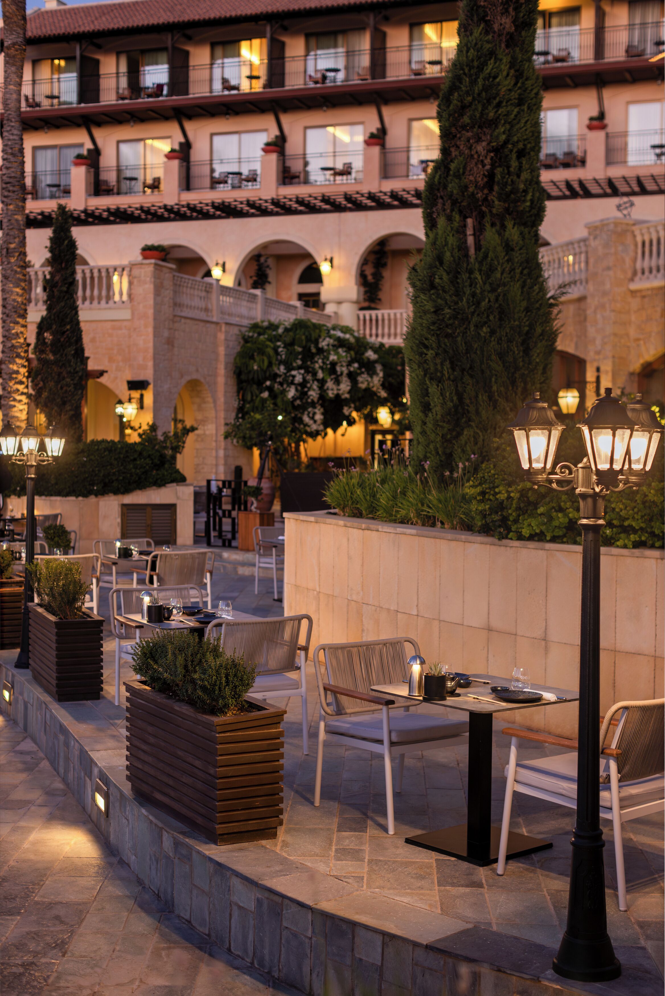 An outdoor patio with tables and chairs, surrounded by planters and a stone wall.