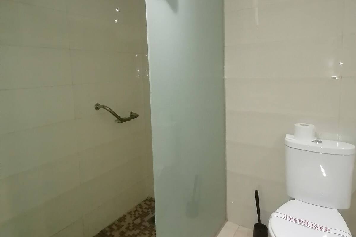 Une salle de bain avec une douche à parois de verre, des toilettes et un sol carrelé.
