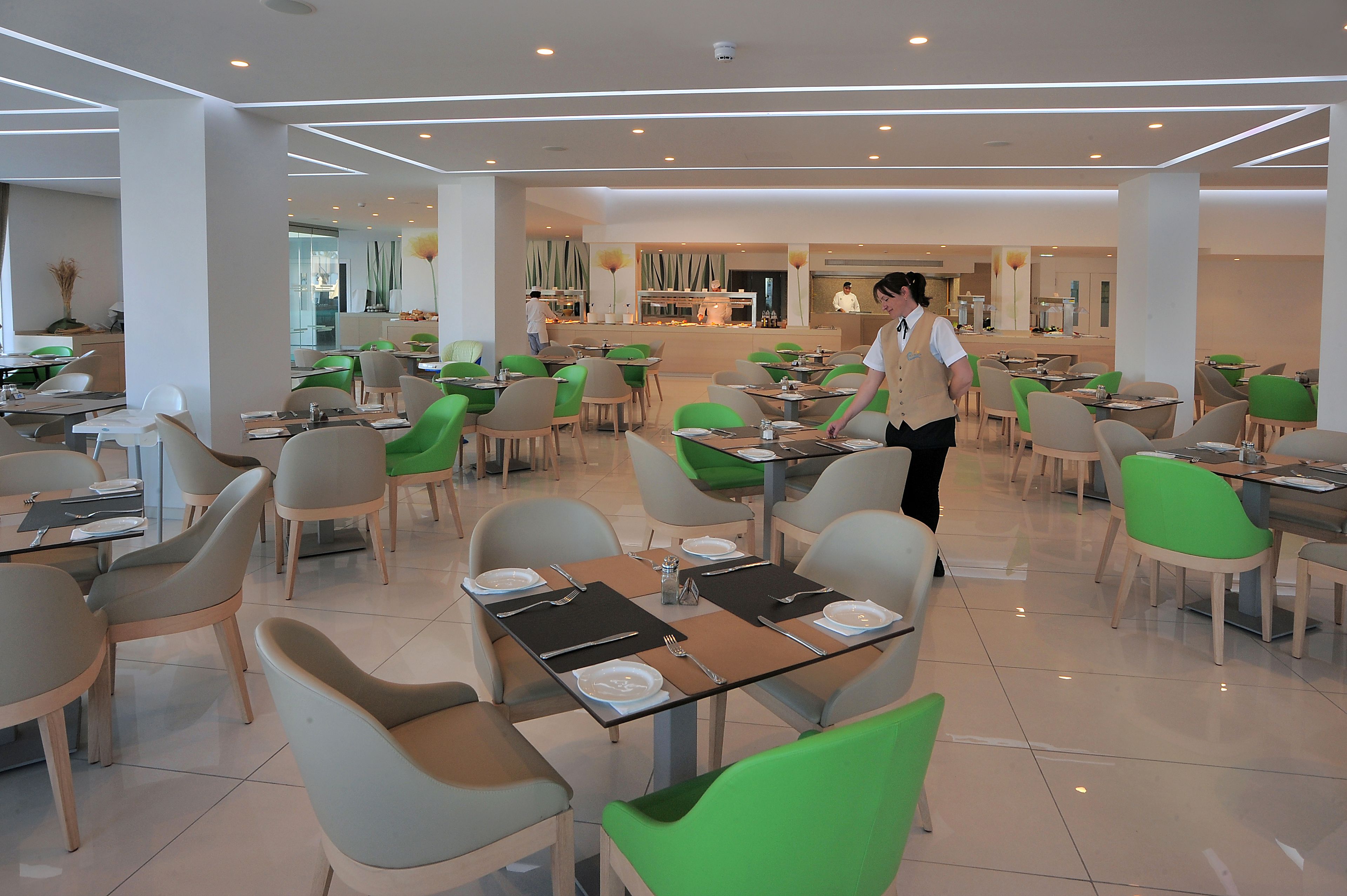 Un área de comedor moderna con varias mesas y sillas, un mostrador central de servicio y un diseño limpio y contemporáneo.