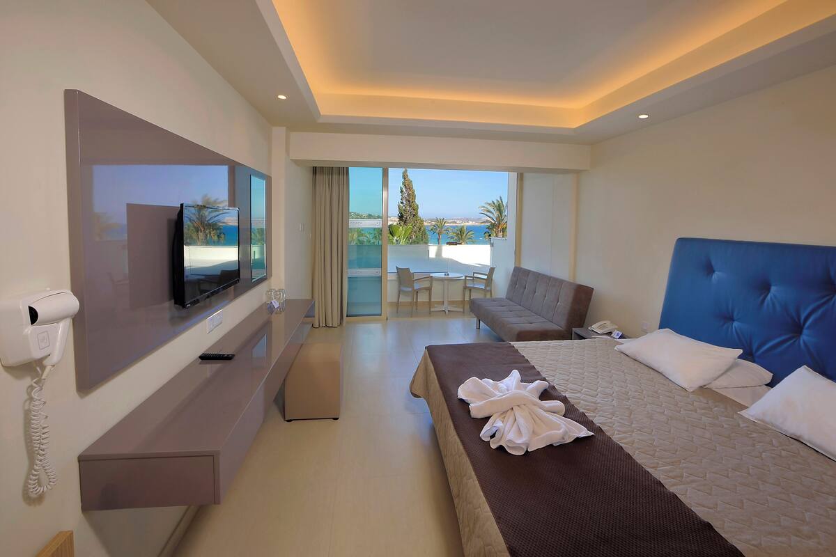 Une chambre d’hôtel équipée d’un lit, d’une télévision, d’un bureau, d’un téléphone et offrant une vue sur la plage.