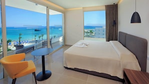 Een hotelkamer met een groot bed, een tafeltje, een stoel en uitzicht op zee en strand.