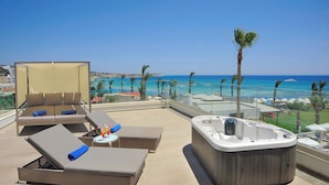 Een terras op het dak met lounge fauteuils, een jacuzzi en uitzicht op het strand en de oceaan.