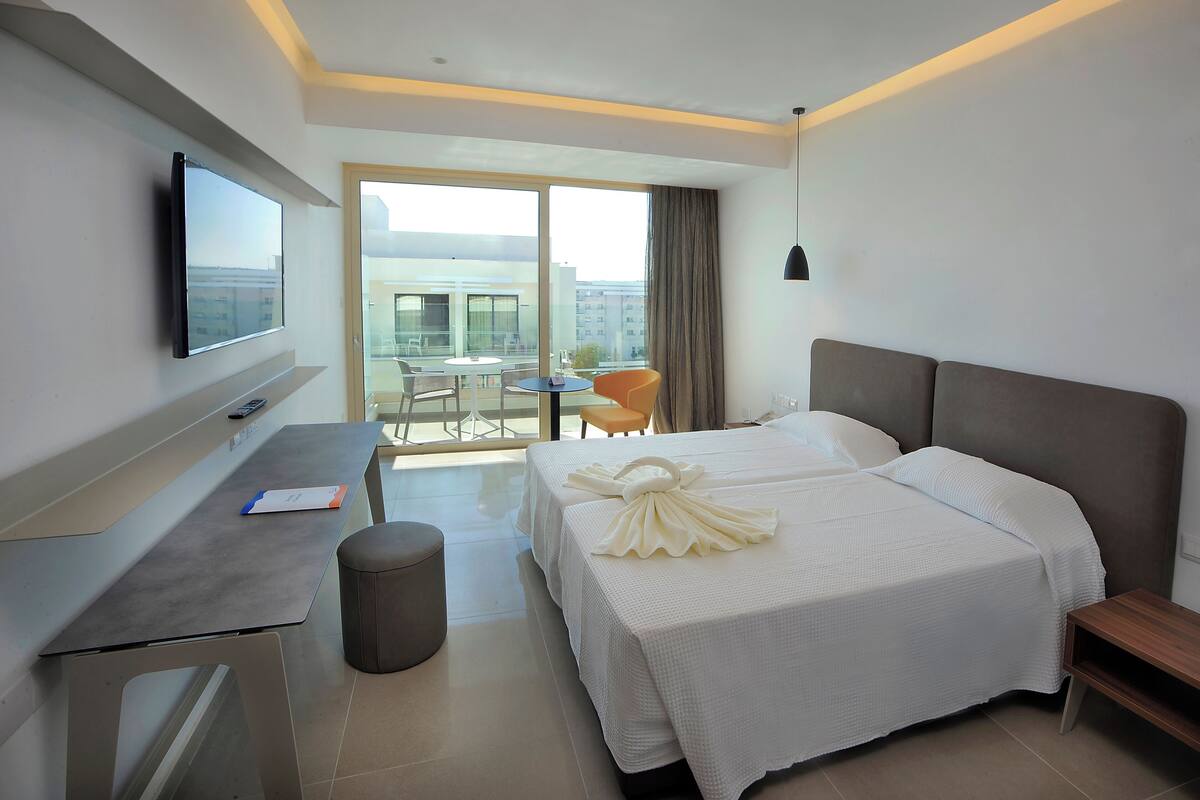 Une chambre d’hôtel comprenant un lit, un bureau, une chaise, une télévision et un balcon avec une table et des chaises.