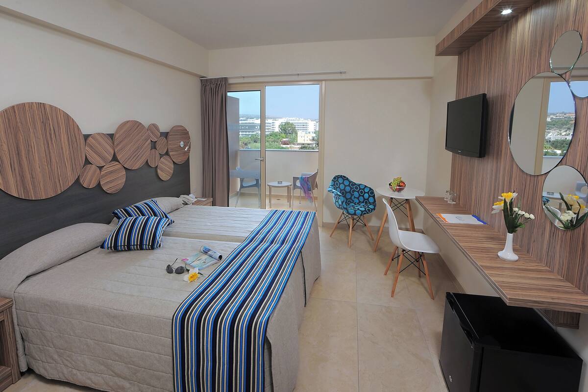 Une chambre d’hôtel avec un lit, un bureau, une télévision et un balcon offrant une vue.