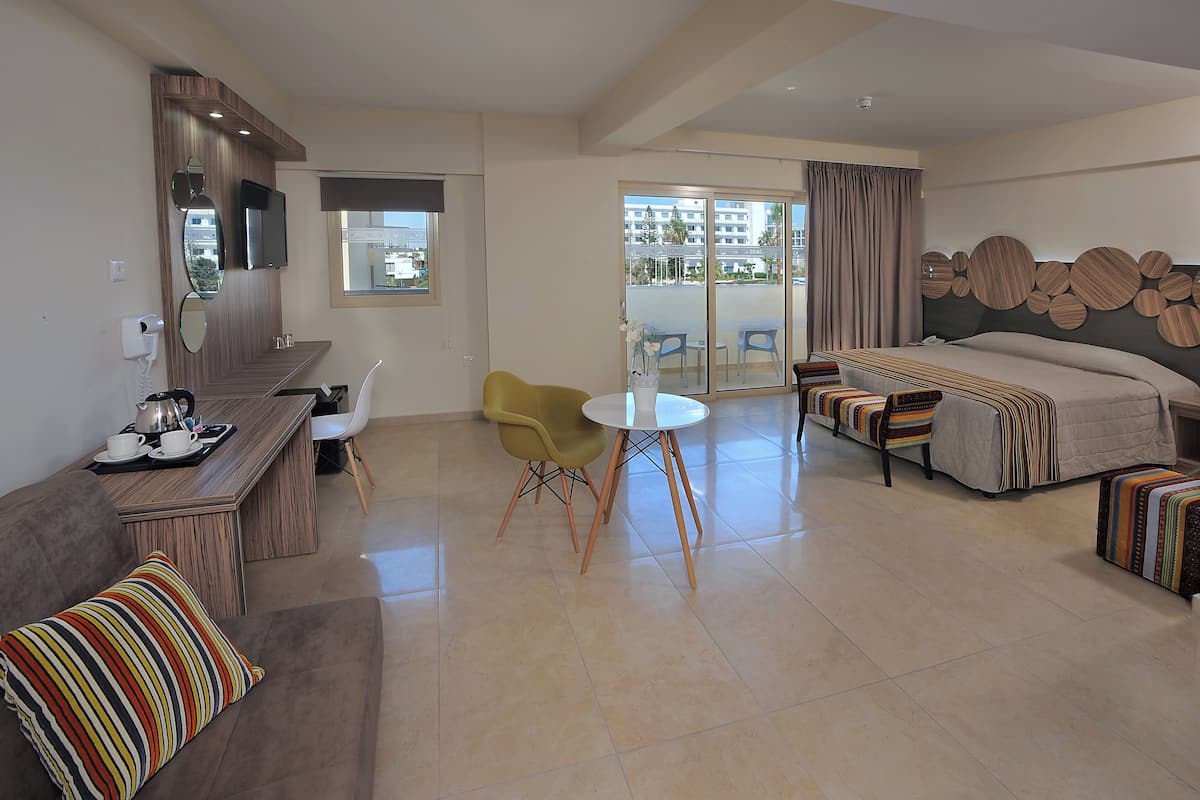 Une chambre d’hôtel comprenant un lit, un canapé, une table à manger avec des chaises, une télévision et un balcon donnant sur des immeubles.