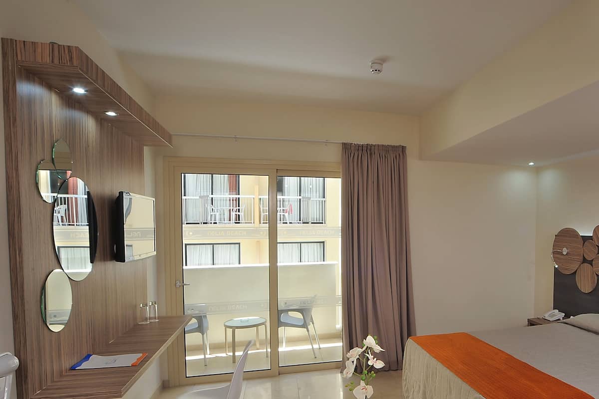 Une chambre d’hôtel comprenant un lit, un bureau avec une chaise, un grand miroir et un balcon donnant sur un immeuble.