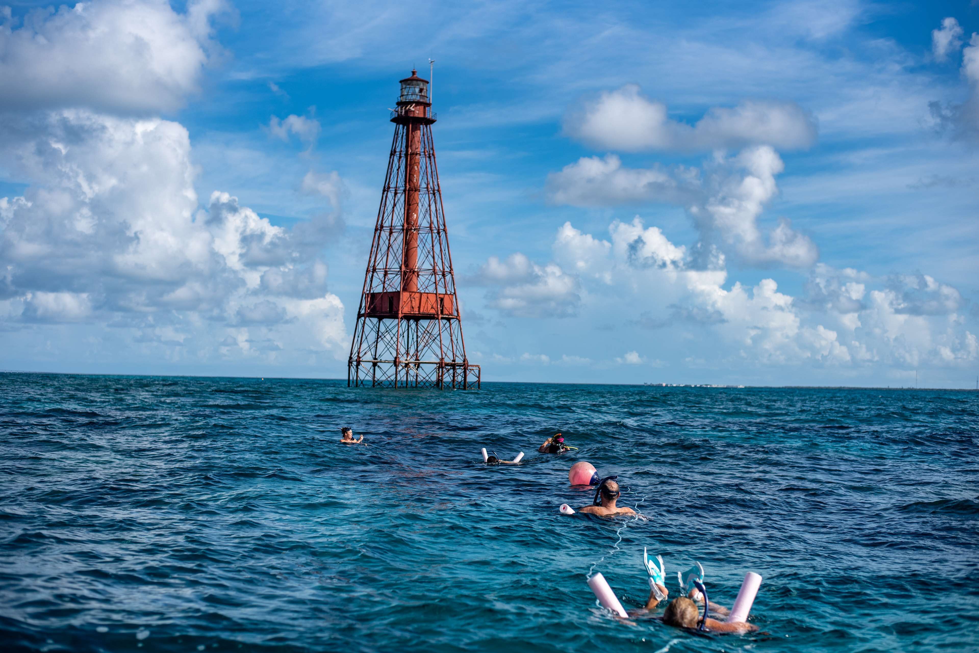 A lighthouse in the background with people swimming in the foreground.