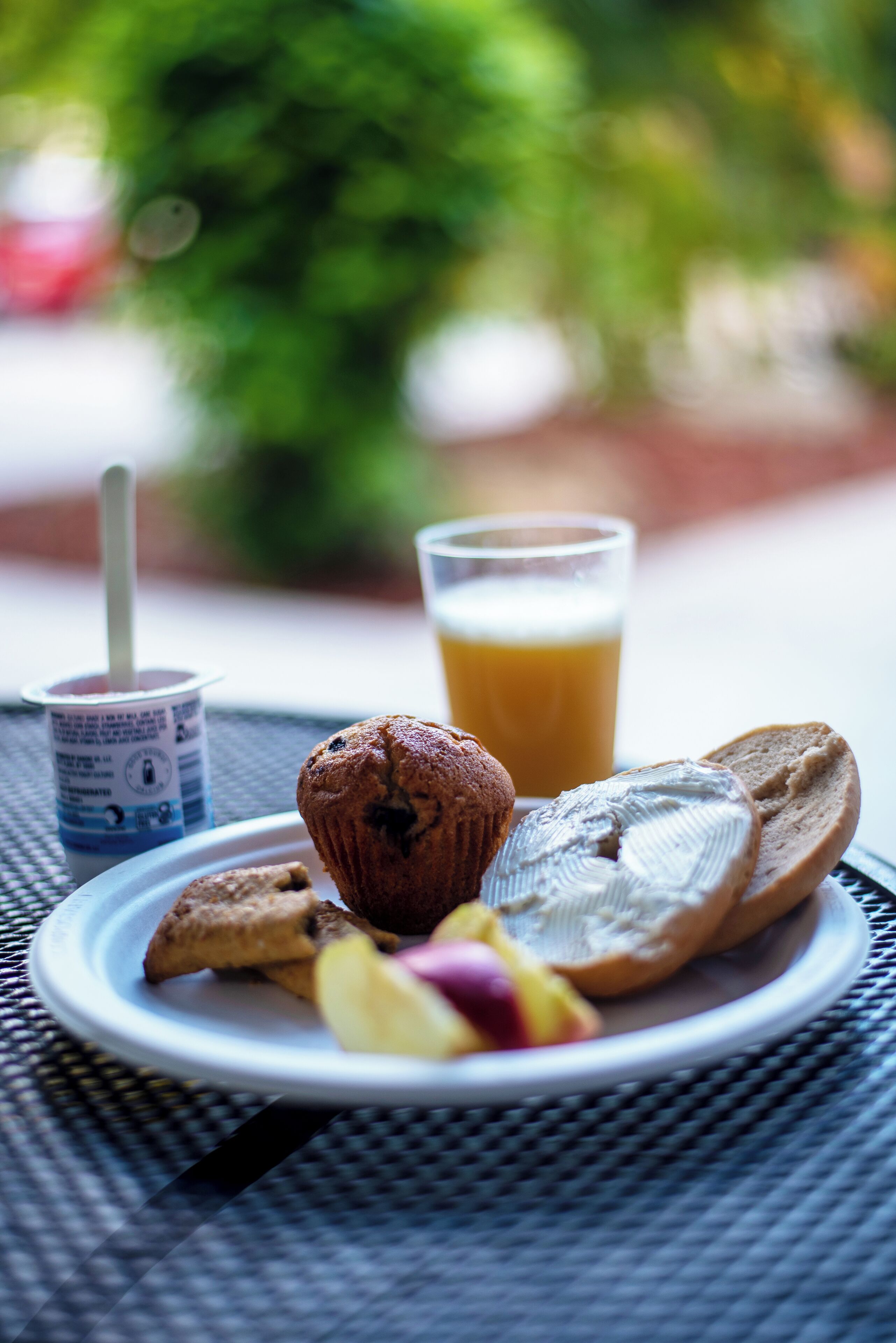 A plate with a muffin, a slice of bread, and some fruit on a table outdoors.