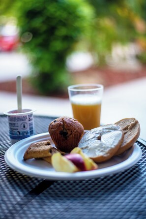 A plate with a muffin, a slice of bread, and some fruit on a table outdoors.