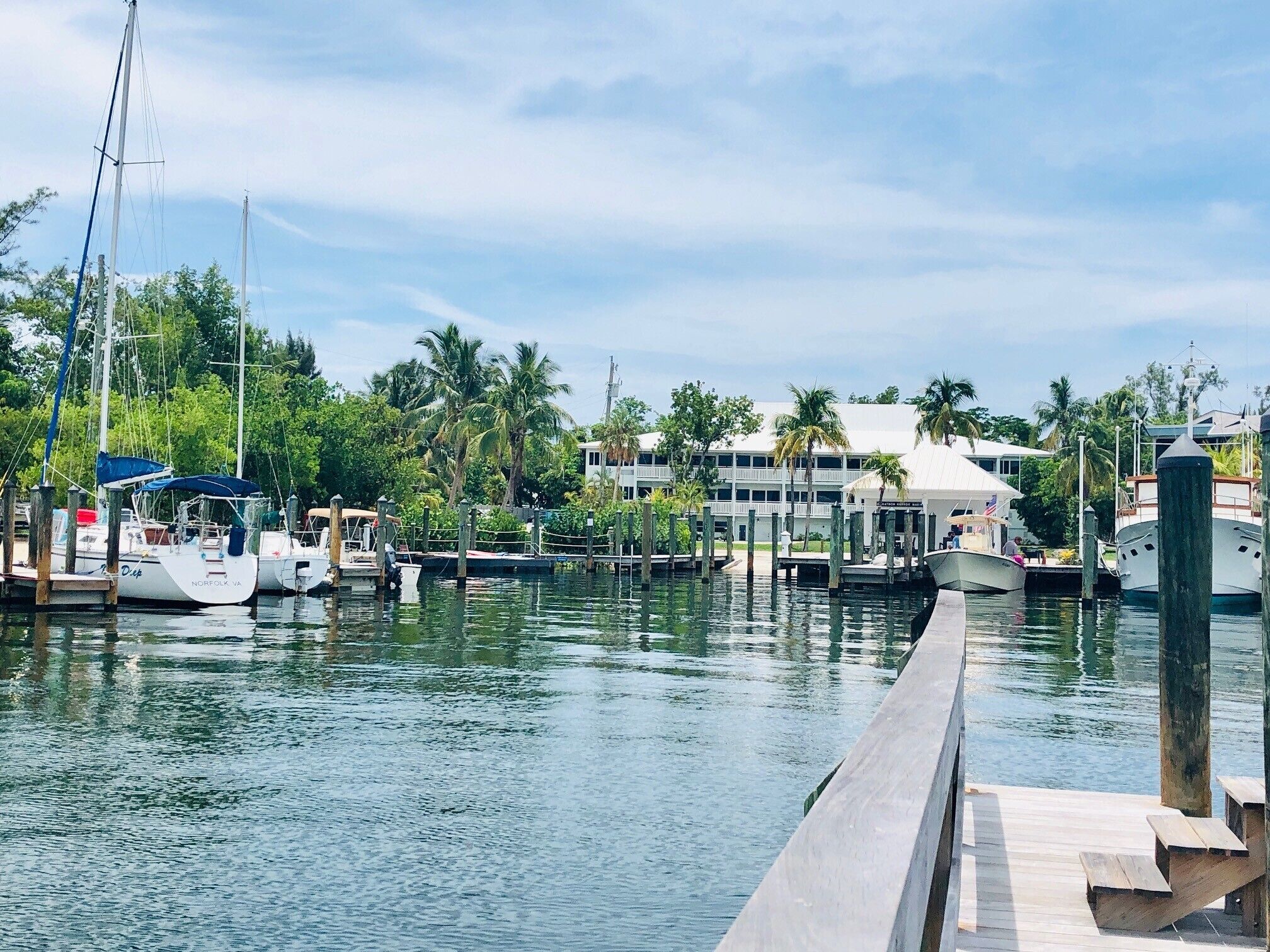 A marina with boats docked, a wooden pier, and a building with a white roof in the background.