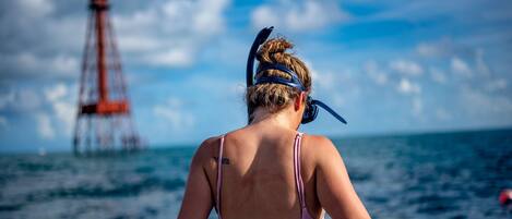 Une personne portant un maillot de bain rose et un bandeau, debout sur un bateau, avec un phare en arrière-plan.