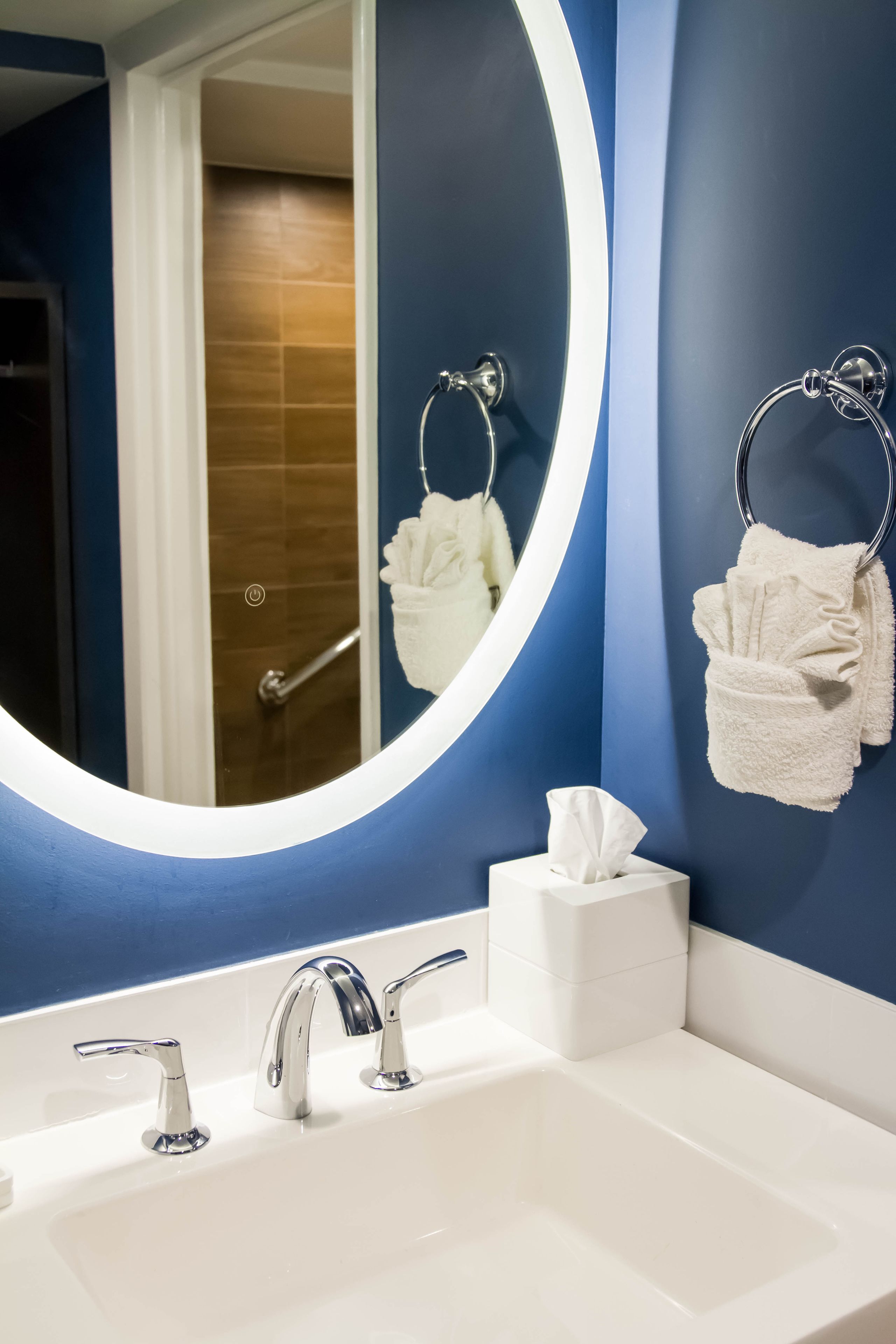 A bathroom with a white sink, chrome faucets, a round mirror, and a towel rack with a white towel.