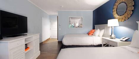 A hotel room with two beds, a television on a white cabinet, a ceiling fan, a decorative mirror, and a painting on the wall.