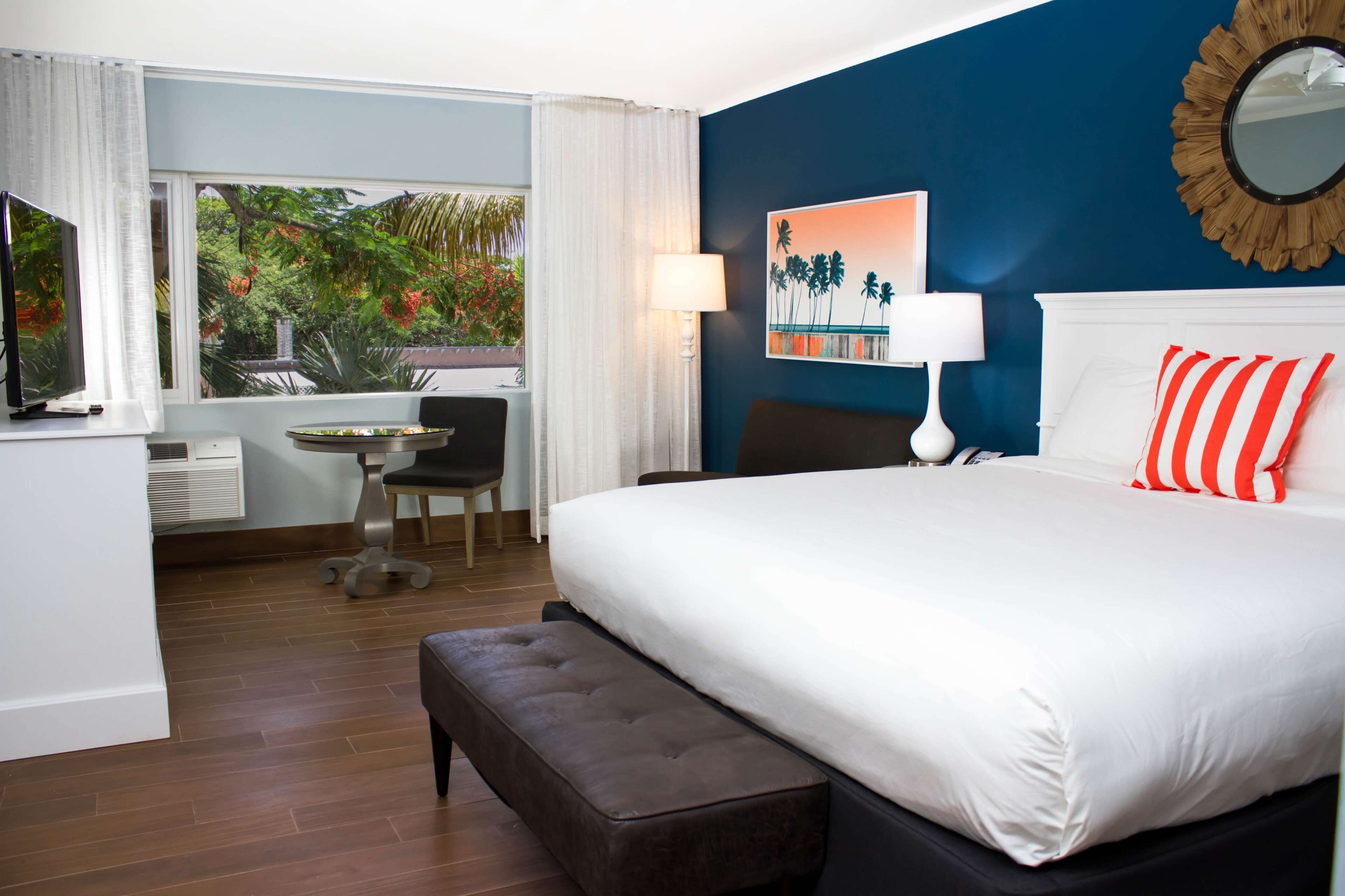 A hotel room with a large bed, a desk, a chair, and a view of greenery outside.