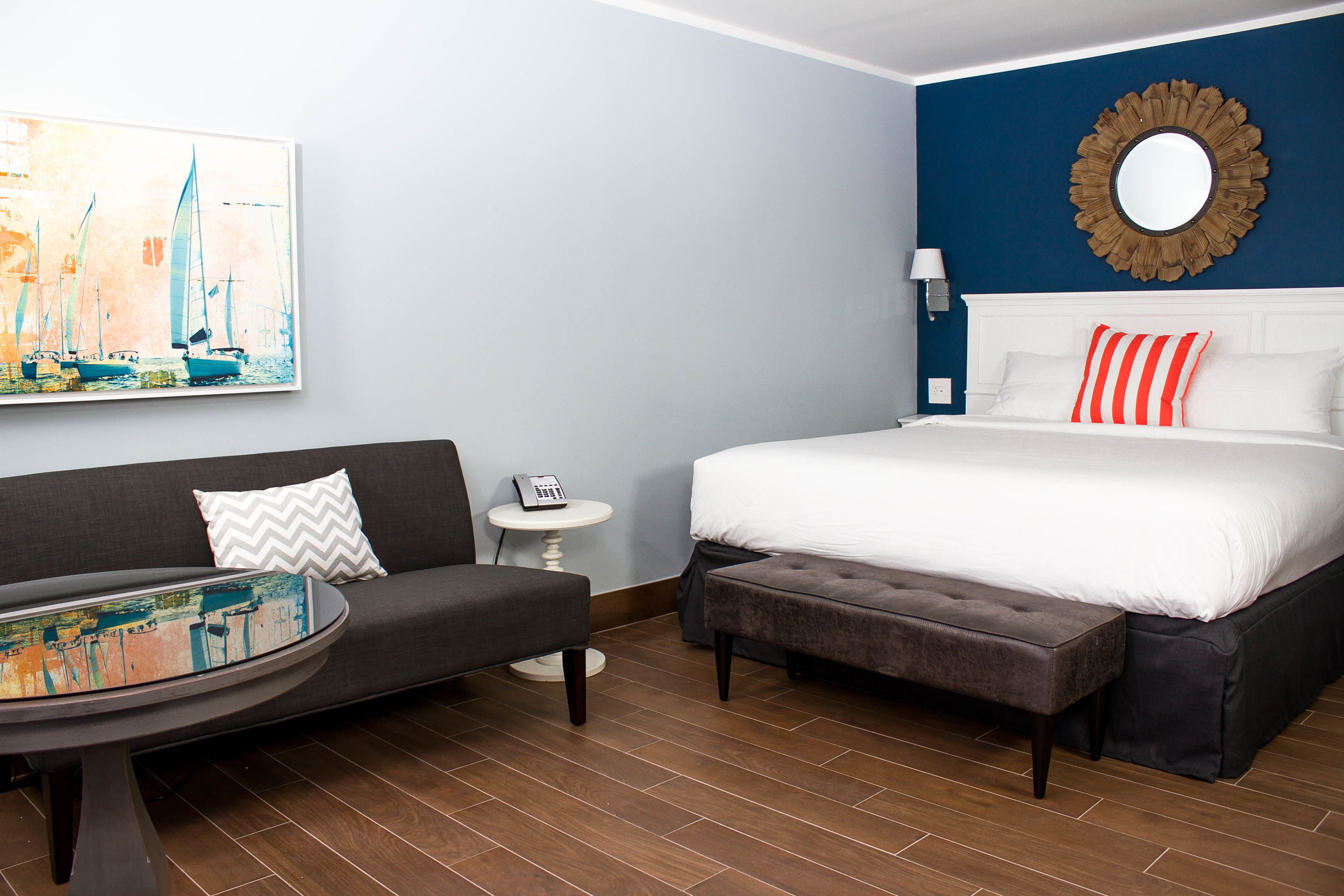 A hotel room with a bed, a sofa, a small table, and a painting on the wall.
