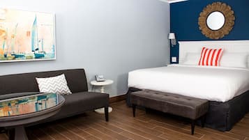 A hotel room with a bed, a sofa, a small table, and a painting on the wall.
