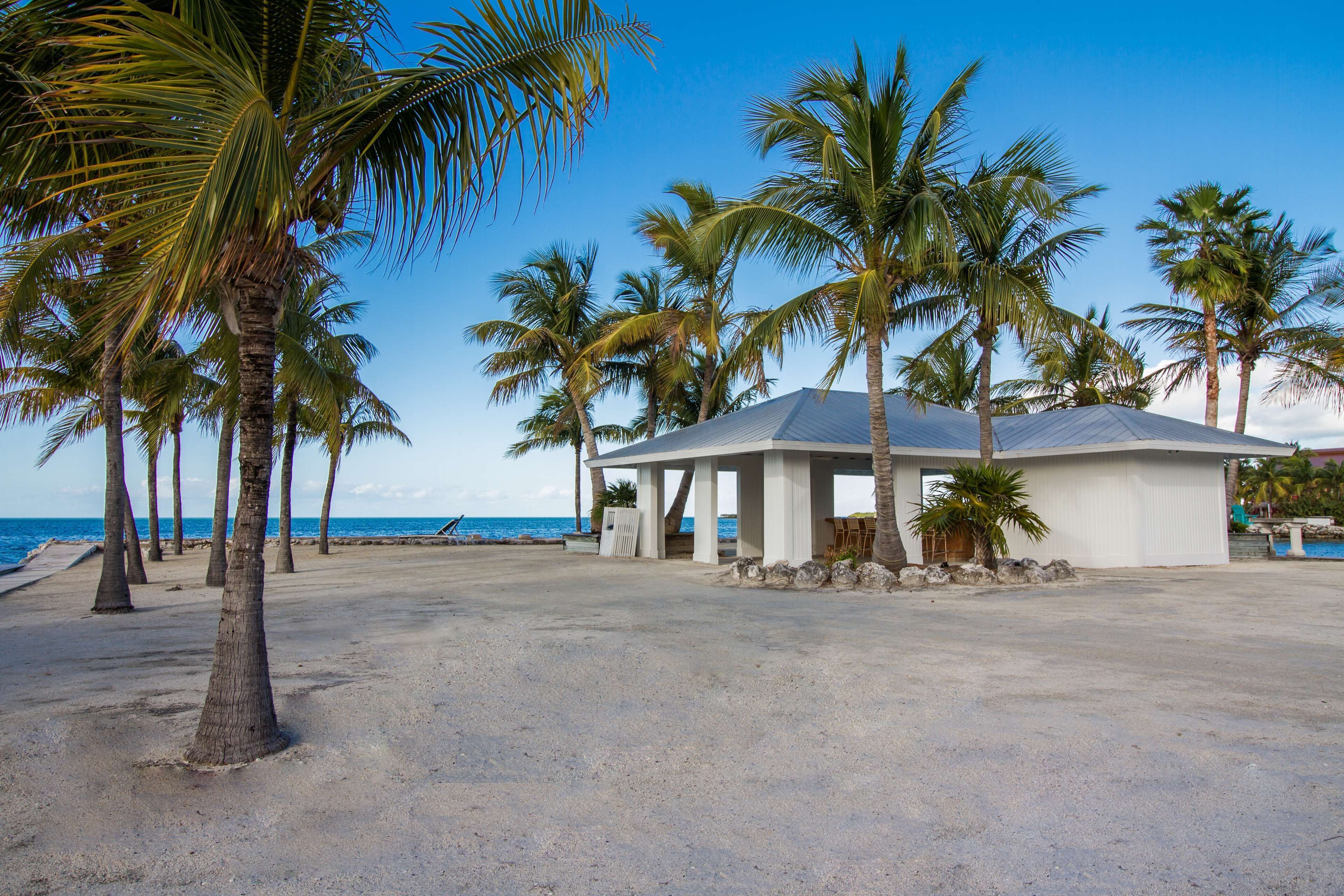 Ein Gebäude direkt am Strand mit einer überdachten Terrasse, Palmen und Blick auf den Ozean.
