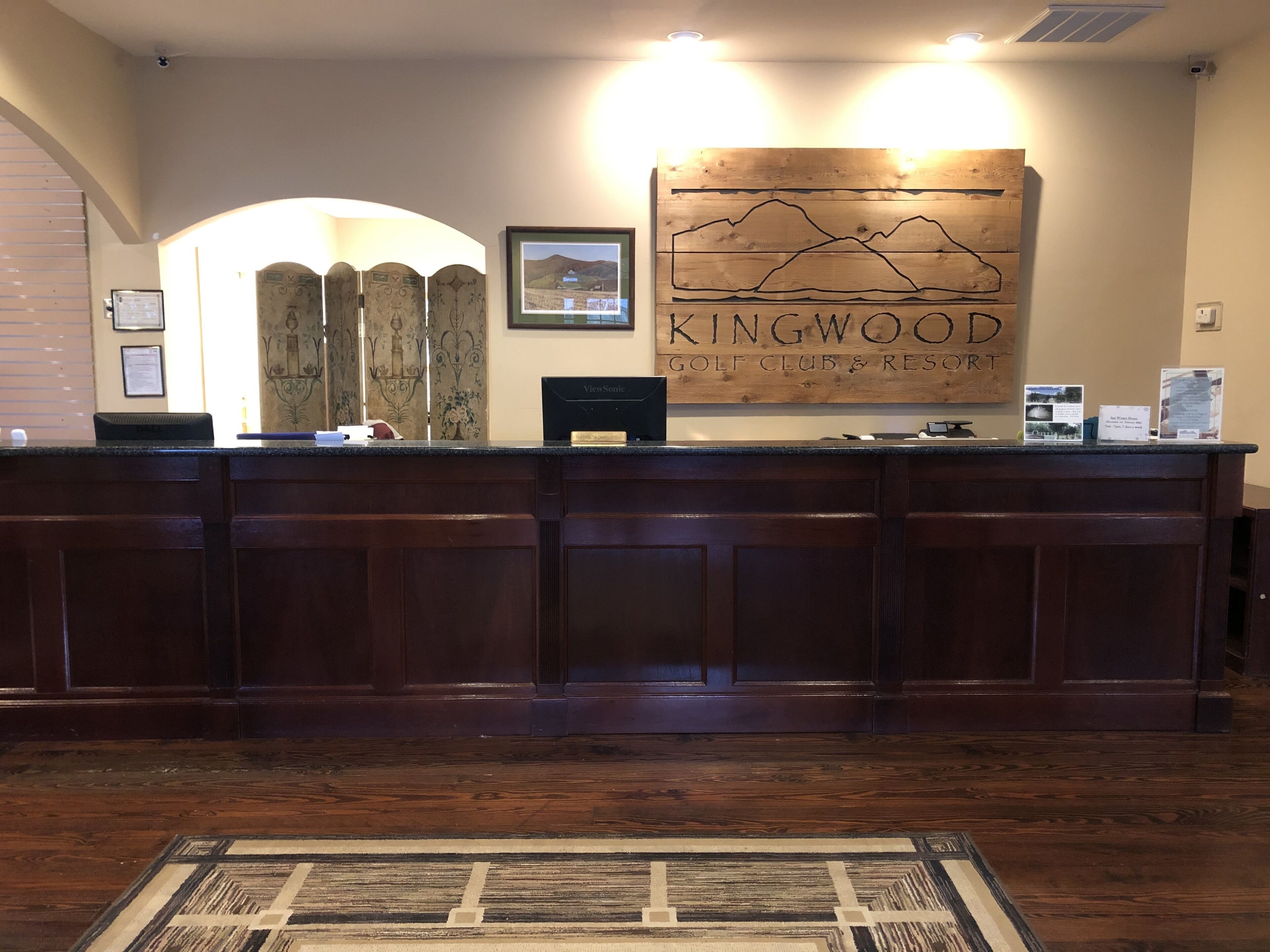 Tauleller de recepció amb un rètol de fusta que diu 'KINGWOOD GOLF CLUB & RESTAURANT' i una fotografia emmarcada a dalt.