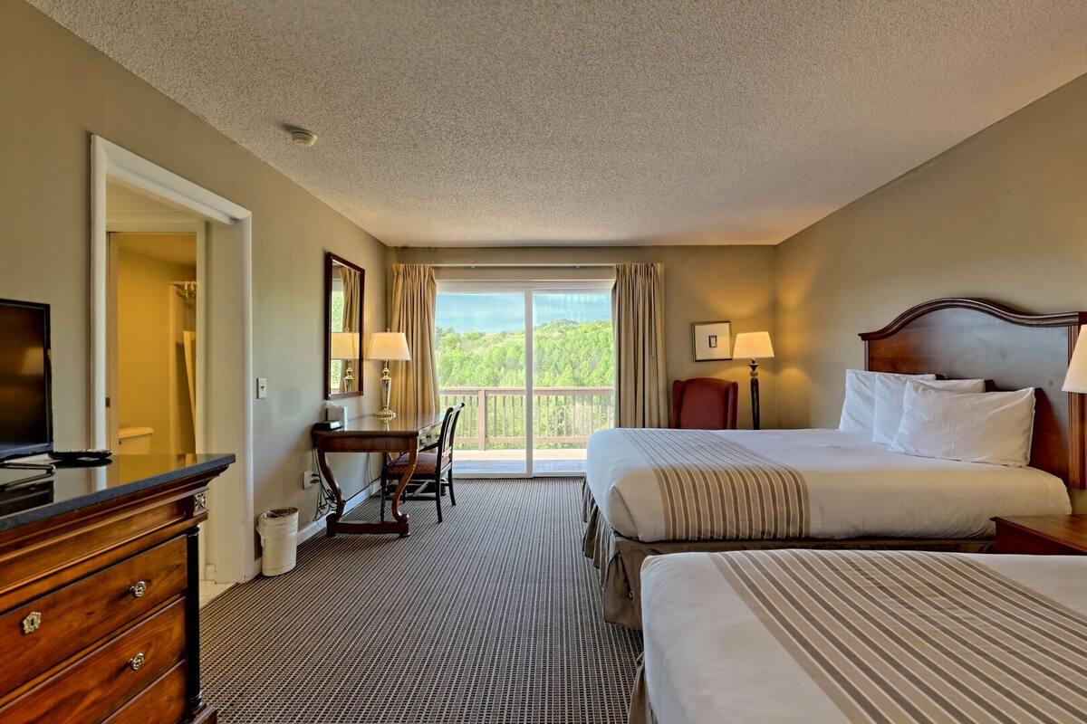A hotel room with a bed, a desk, a chair, a television, and a view of the outdoors.