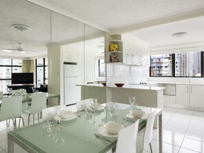 A modern hotel room with a dining area, kitchen, and a large window offering a city view. - BreakFree Beachpoint (Surfers Paradise)